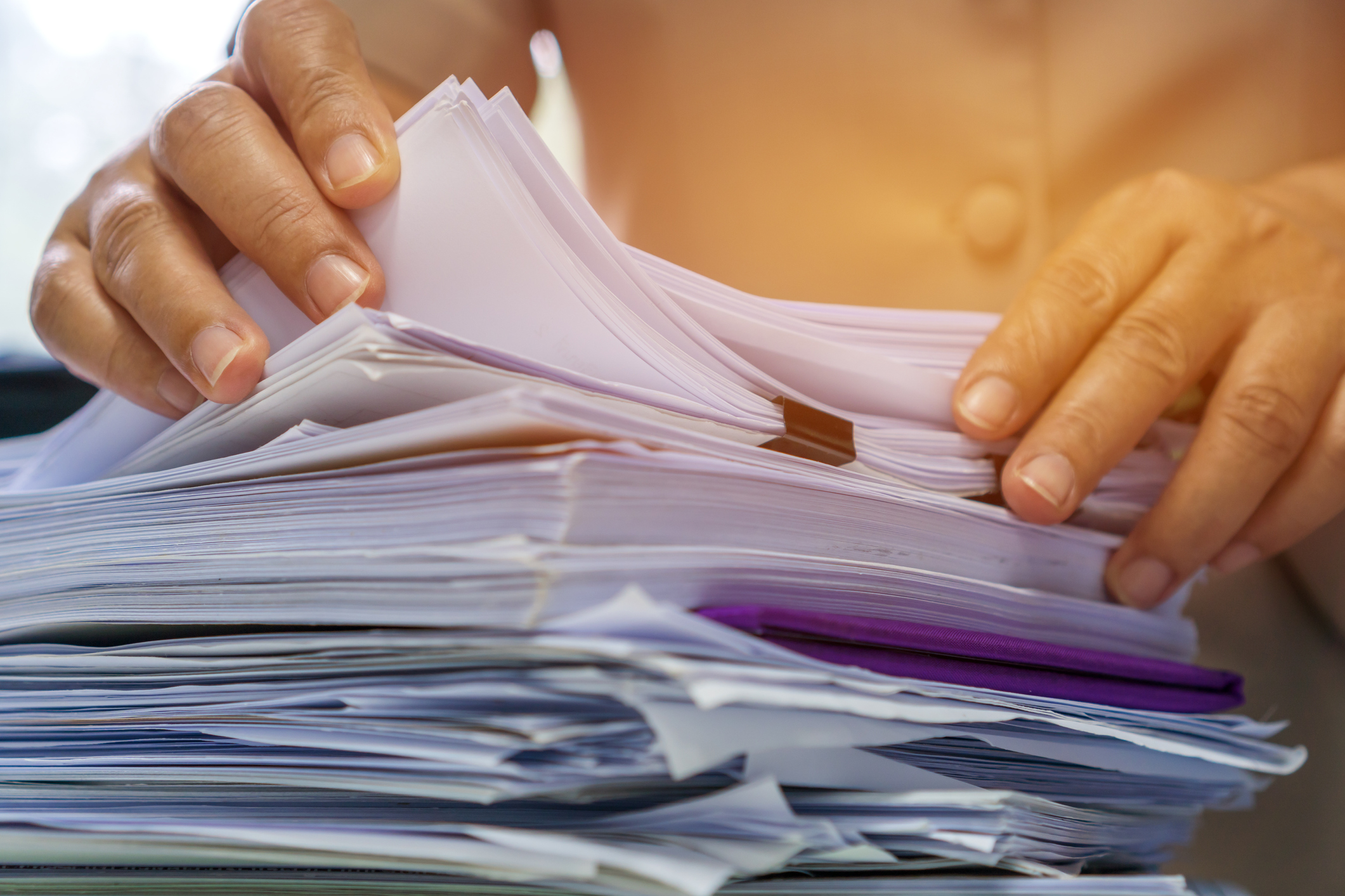 A person sorting through insurance paperwork and certificates piled on a desk.